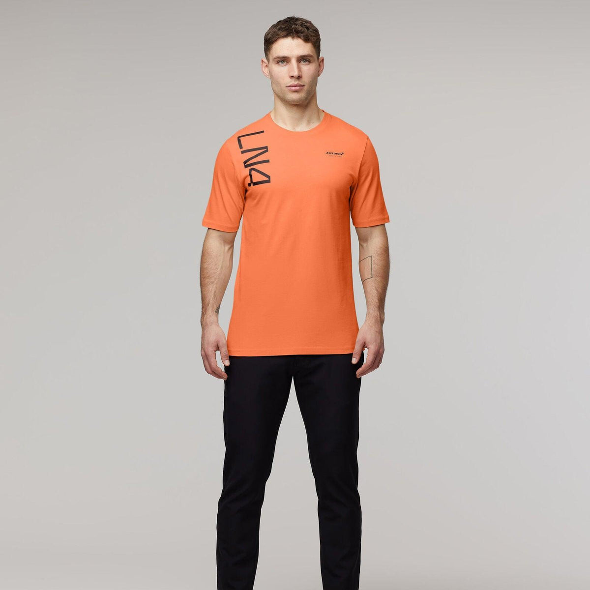 Man wearing an orange McLaren F1 Lando Norris Core T-shirt and black pants.