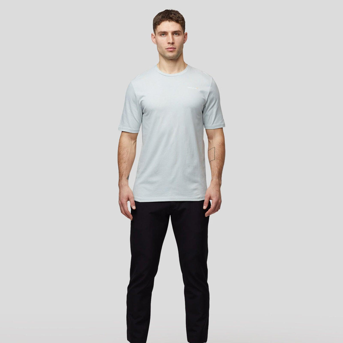 Man wearing a light blue McLaren F1 Lando Norris Core Essentials T-shirt and black trousers.